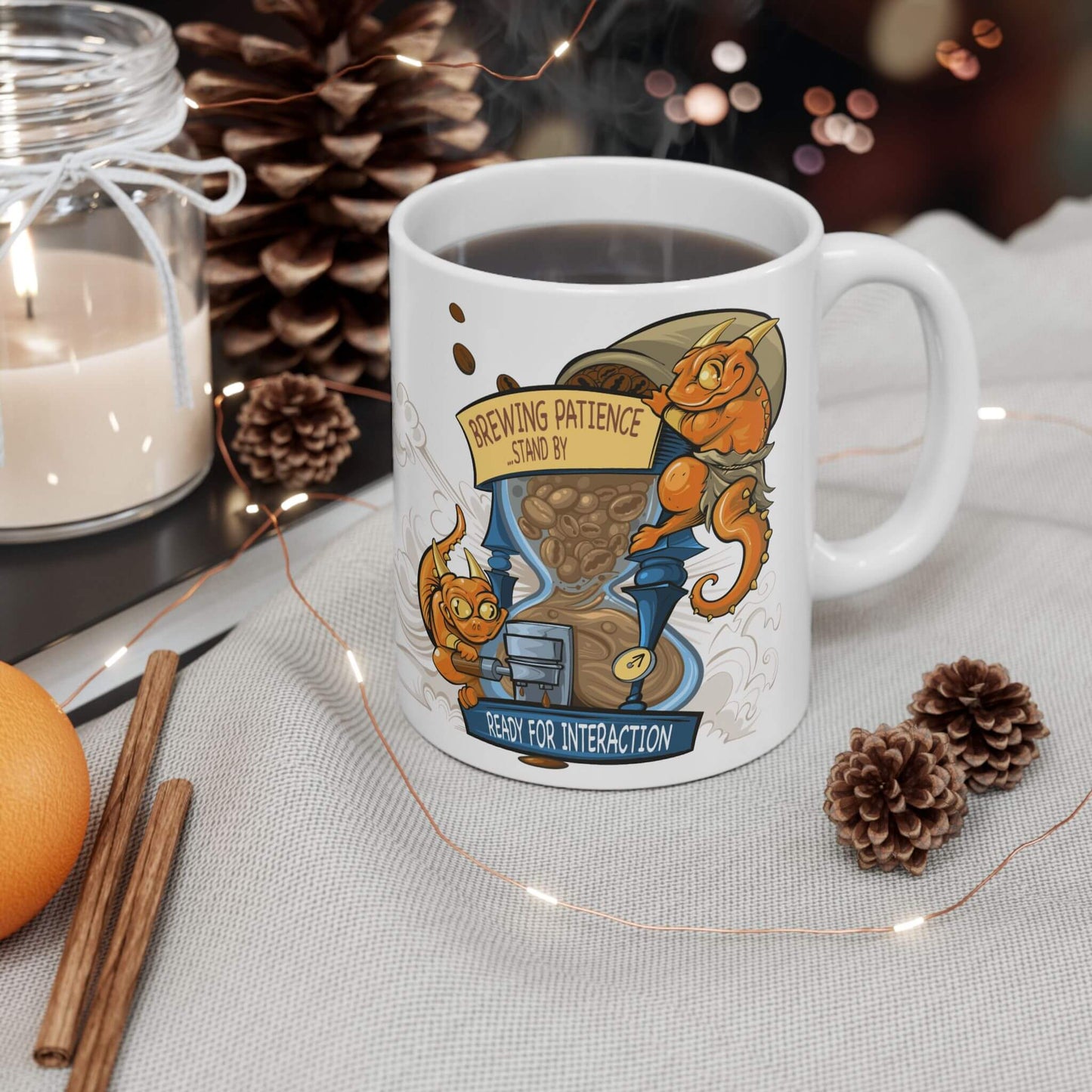 White mug with a cartoon design featuring kobolds and an hourglass with coffee beans and text, surrounded by decorative items on a table.