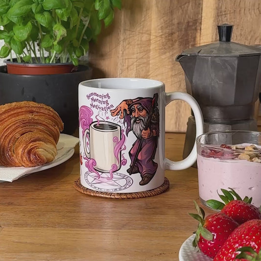 Video showcasing GeekyGearing's 'Summoning Morning Motivation Mug' in a breakfast setting with a croissant, yogurt with toppings, and strawberries. The clip begins a zoom into the mug, followed with the mug rotating to reveal all angles and then cuts to a separate shot of coffee being poured into it.
