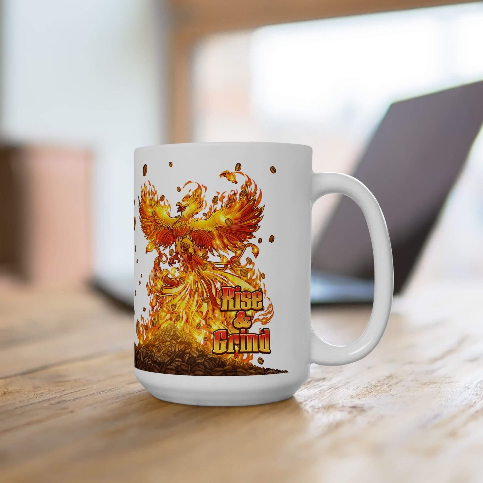White mug with a phoenix rising from a pile of coffee beans design and 'Rise and Grind' text on a wooden surface.