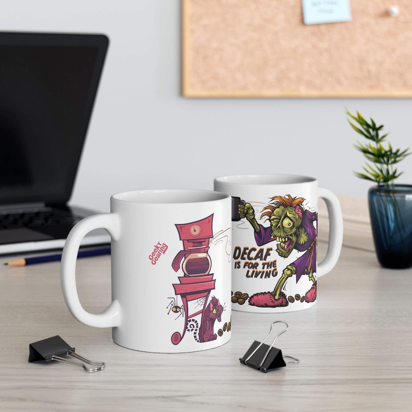 Two mugs with cartoon designs on a desk with office supplies and a plant.