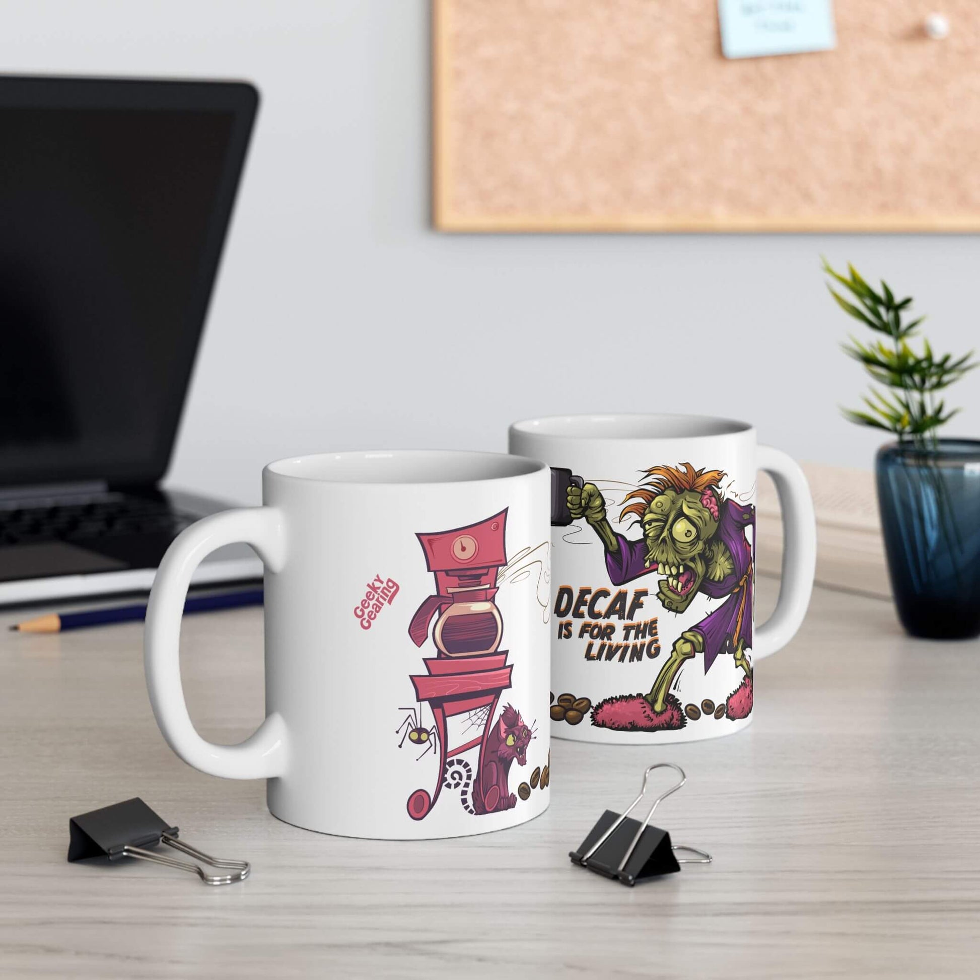 Two mugs with cartoon designs on a desk with office supplies and a plant.