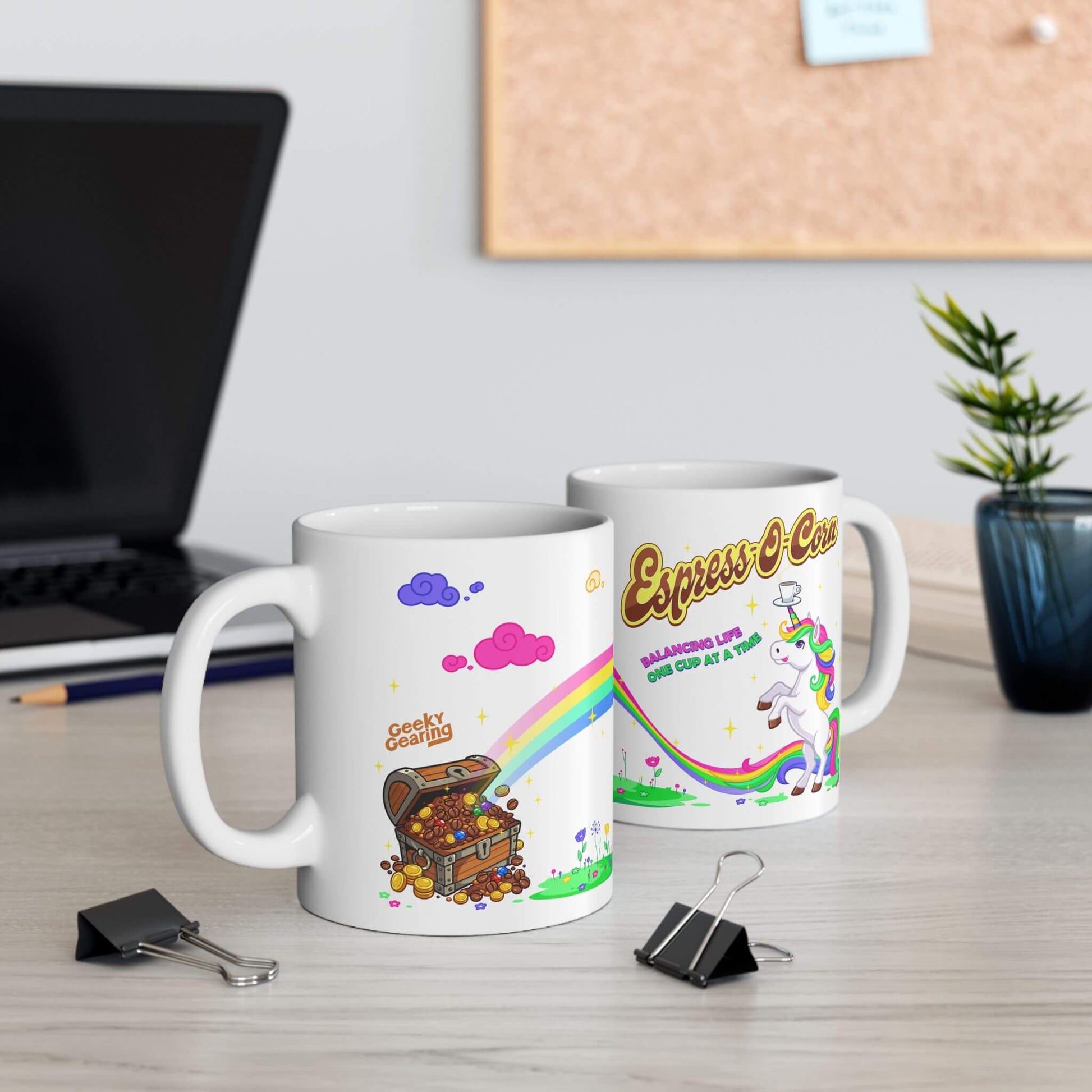 Two mugs with colorful designs on a desk with office supplies and a plant.