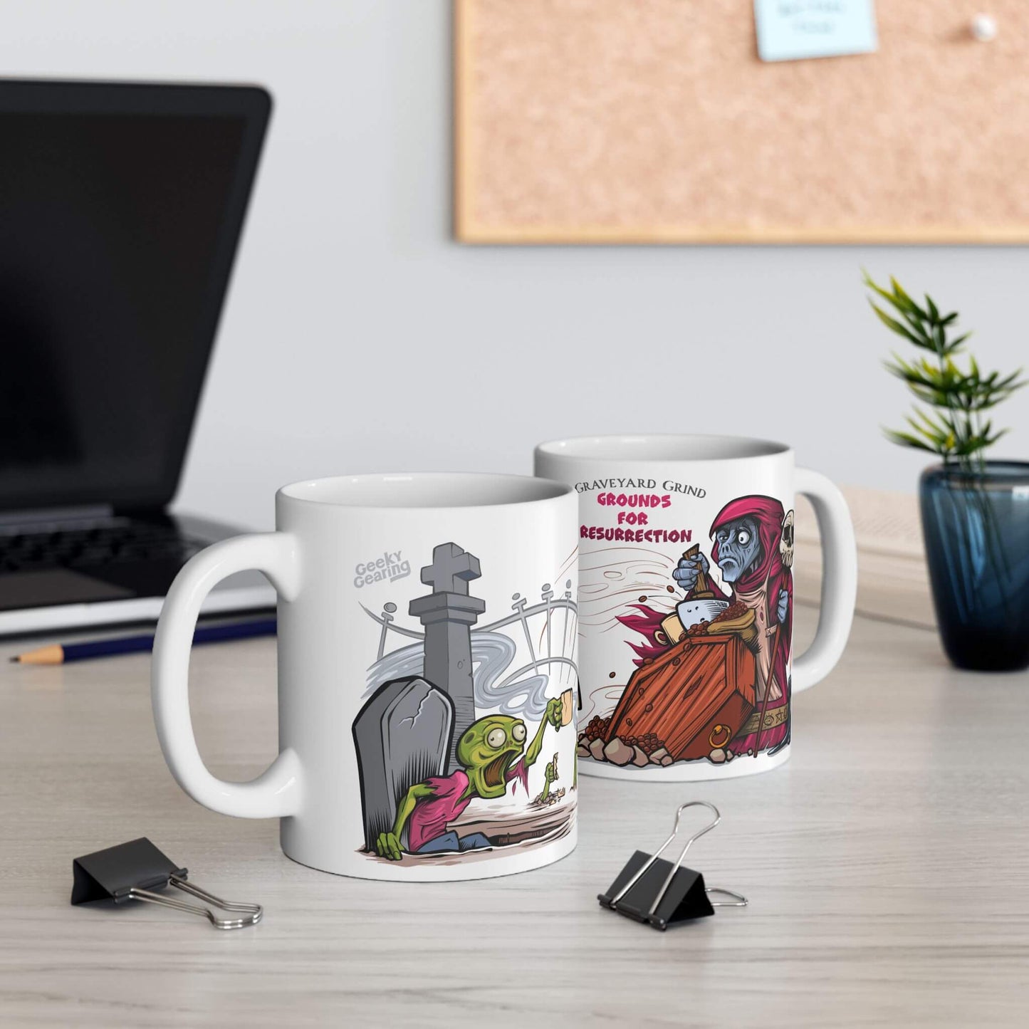 Two mugs with cartoon designs on a desk with a laptop and plant in the background