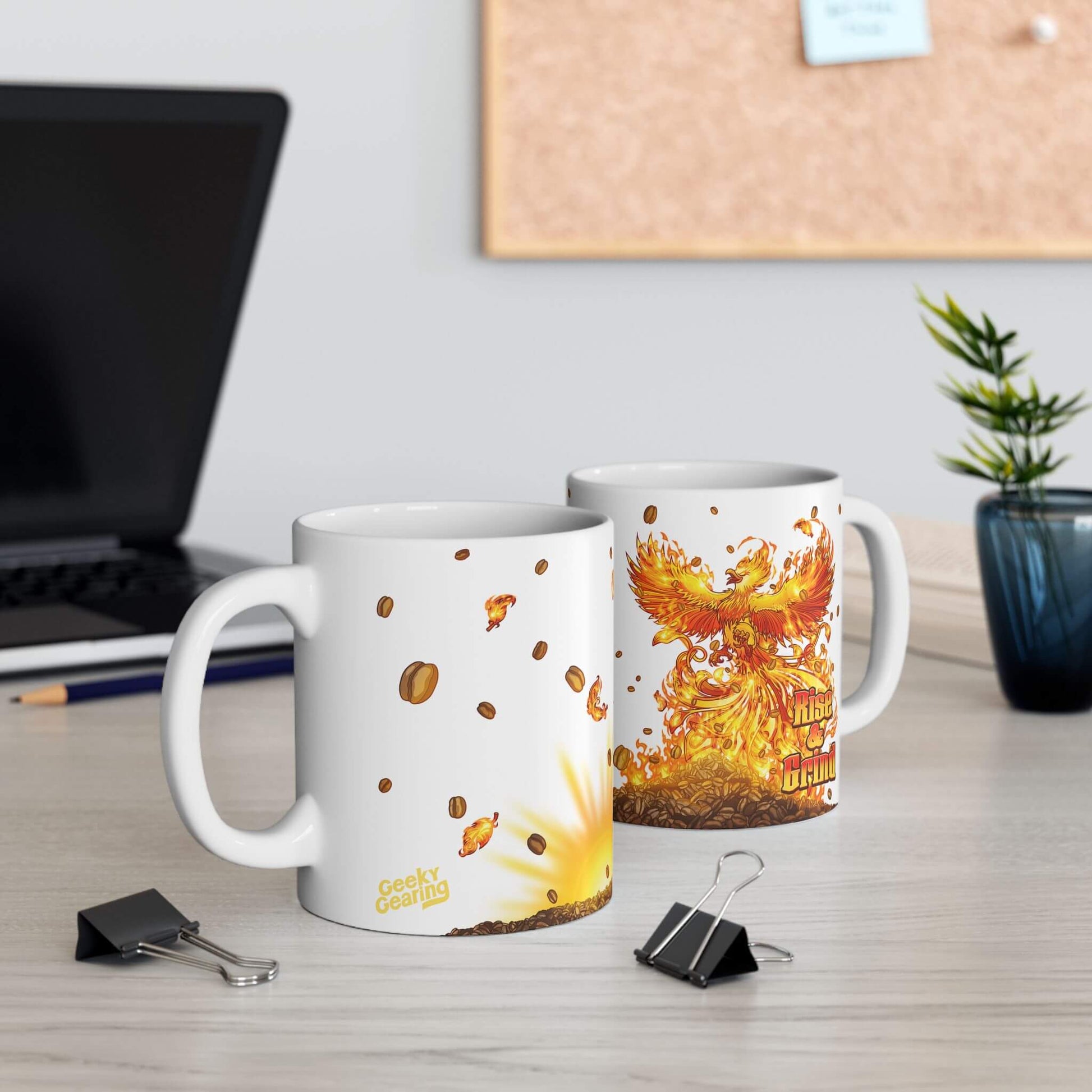 Two mugs with fiery designs on a desk with a laptop and plant in the background