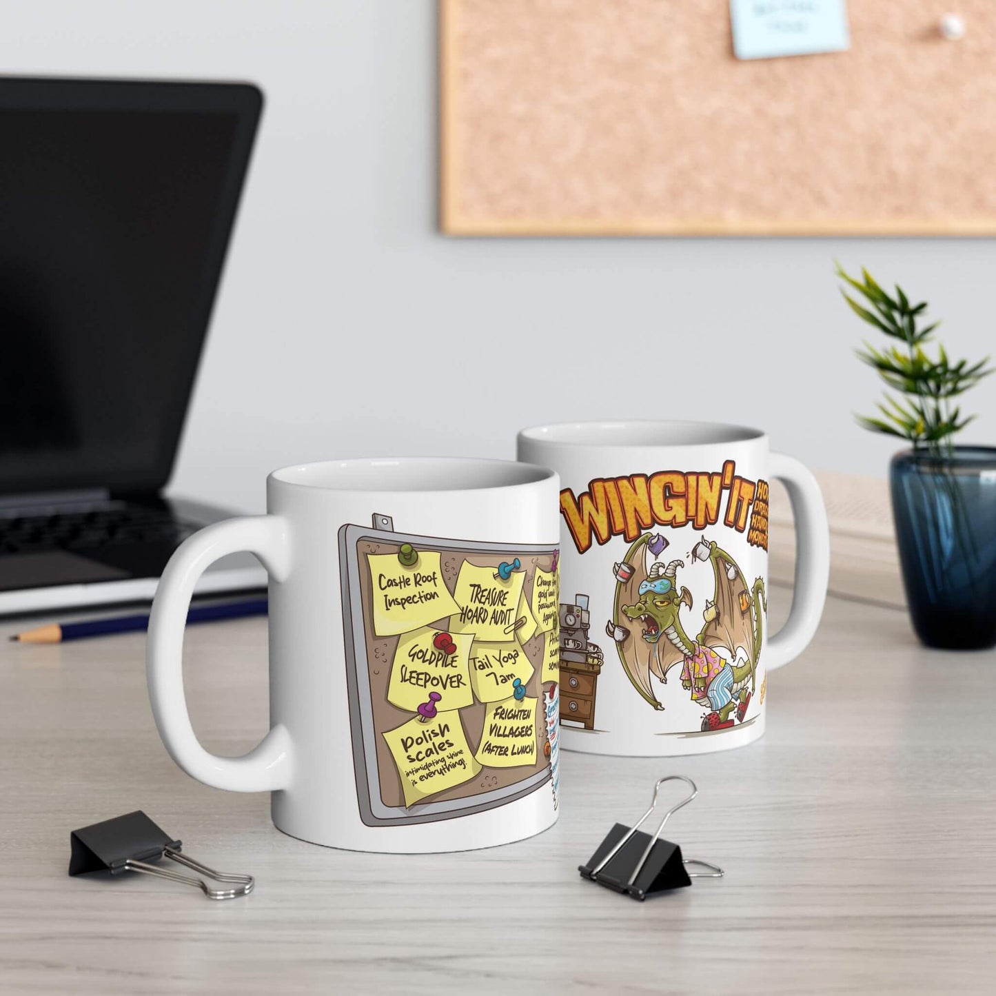 Two mugs on a desk with cartoon designs, one featuring a corkboard with notes and the other with a cartoon dragon.