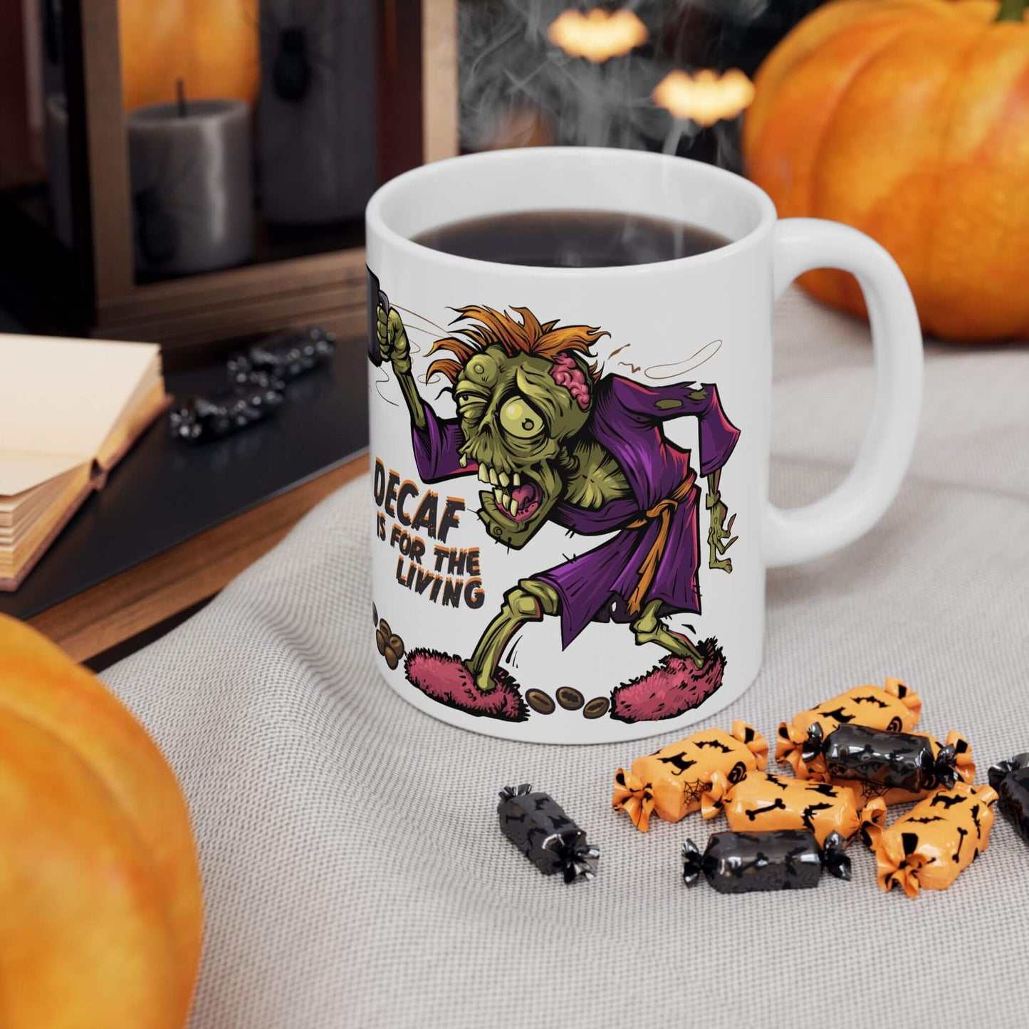 Mug with Halloween-themed design featuring a zombie and text, surrounded by pumpkins and candies on a table.