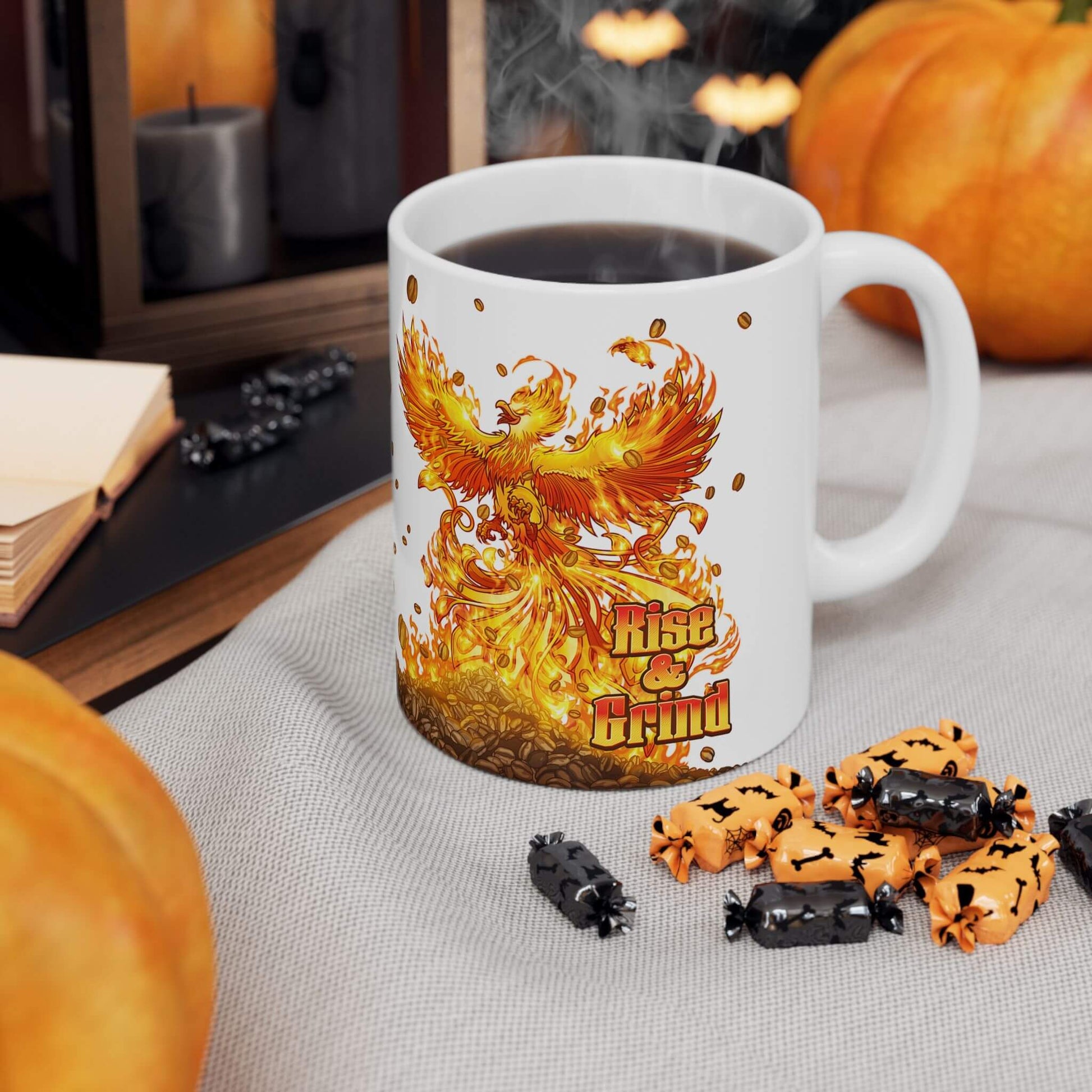 Mug with phoenix design and text 'Rise and Grind' on a table with pumpkins and treats.
