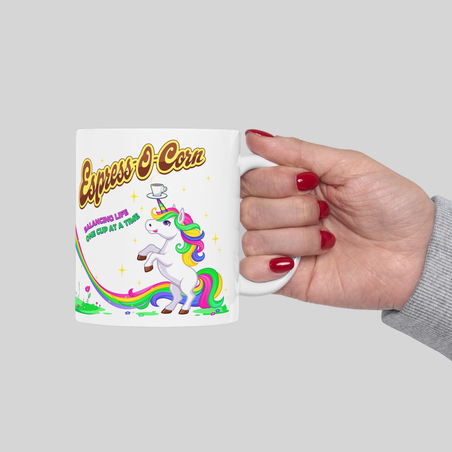 Mug with a unicorn design and text held by a hand on a gray background