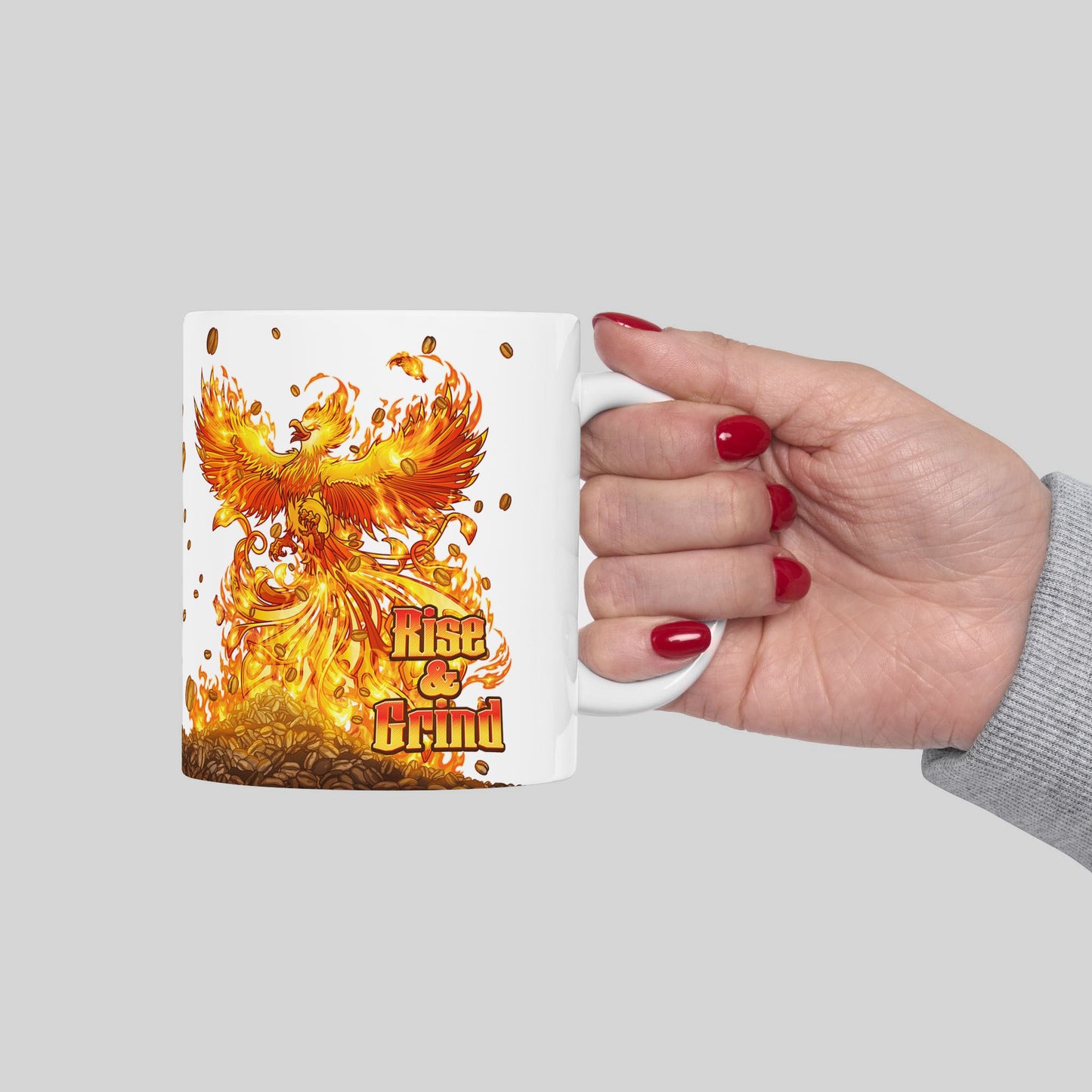 Mug with a phoenix design and 'Rise & Grind' text held by a hand on a gray background