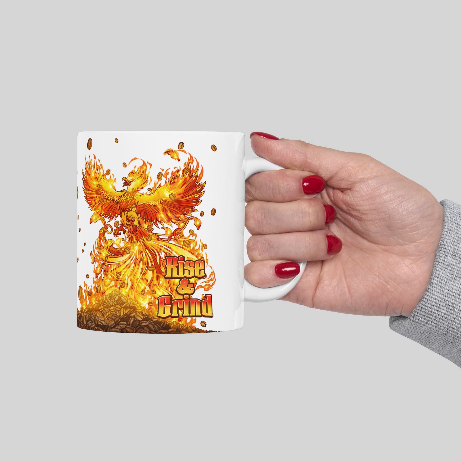 Mug with a phoenix design and 'Rise & Grind' text held by a hand on a gray background
