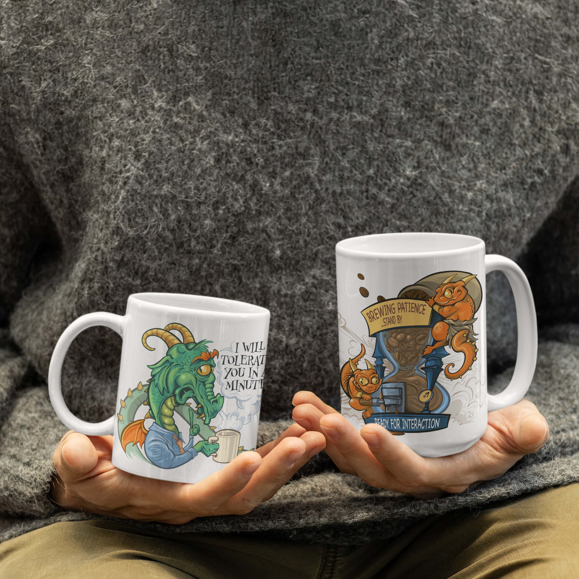 An 11 oz and 15 oz version of the Tolerance Timer mug held in hand by a person. The graphic on the mug shows a tired dragon who clearly needs his coffee before he can deal with people.