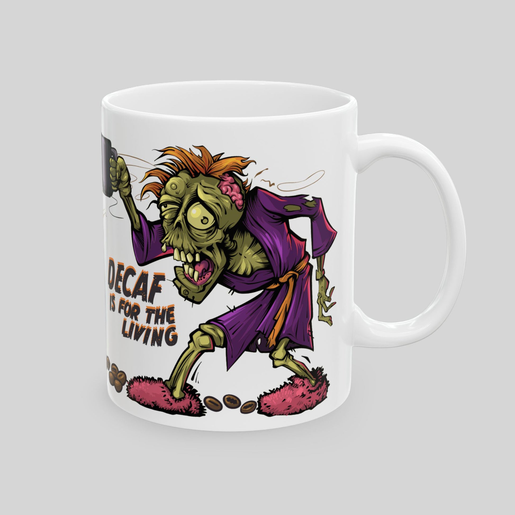 White 11 oz ceramic mug with cartoon zombie holding coffee; text: “Decaf is for the Living”