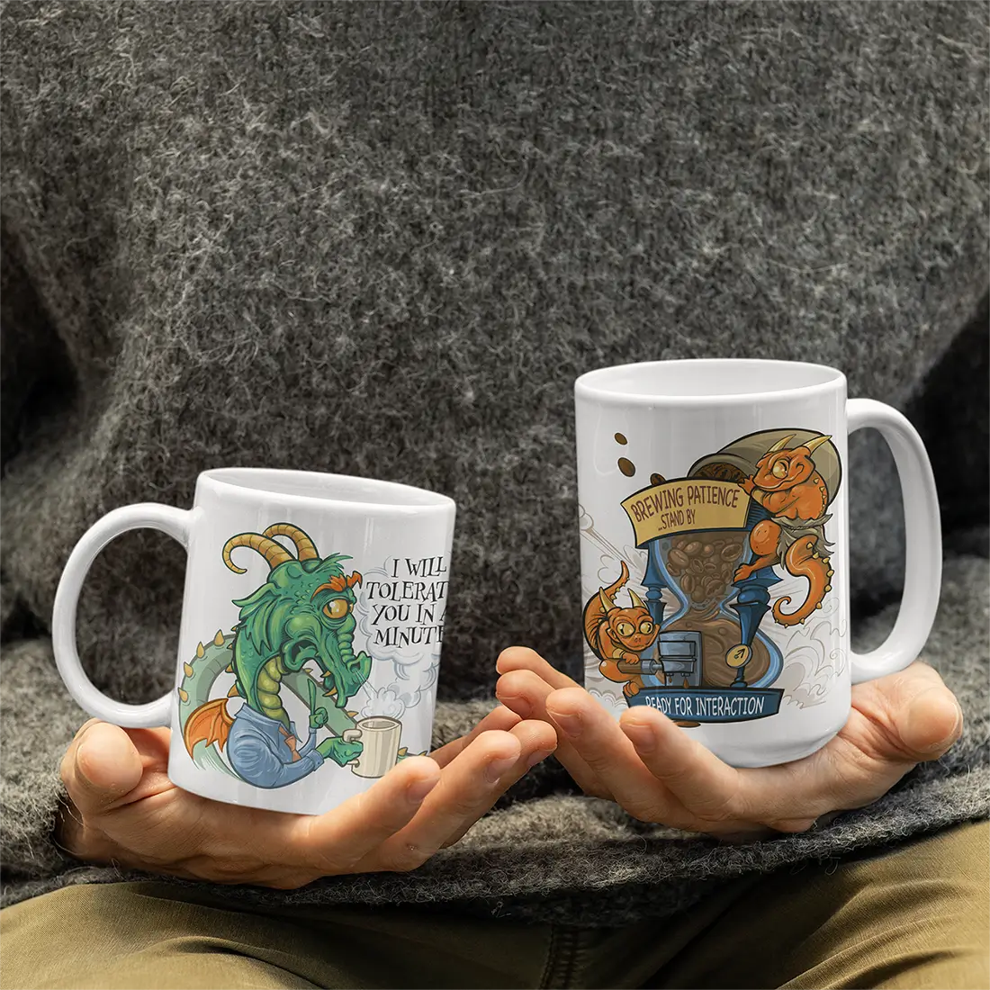 An 11 oz and 15 oz version of the Tolerance Timer mug held in hand by a person. The graphic on the mug shows a tired dragon who clearly needs his coffee before he can deal with people.